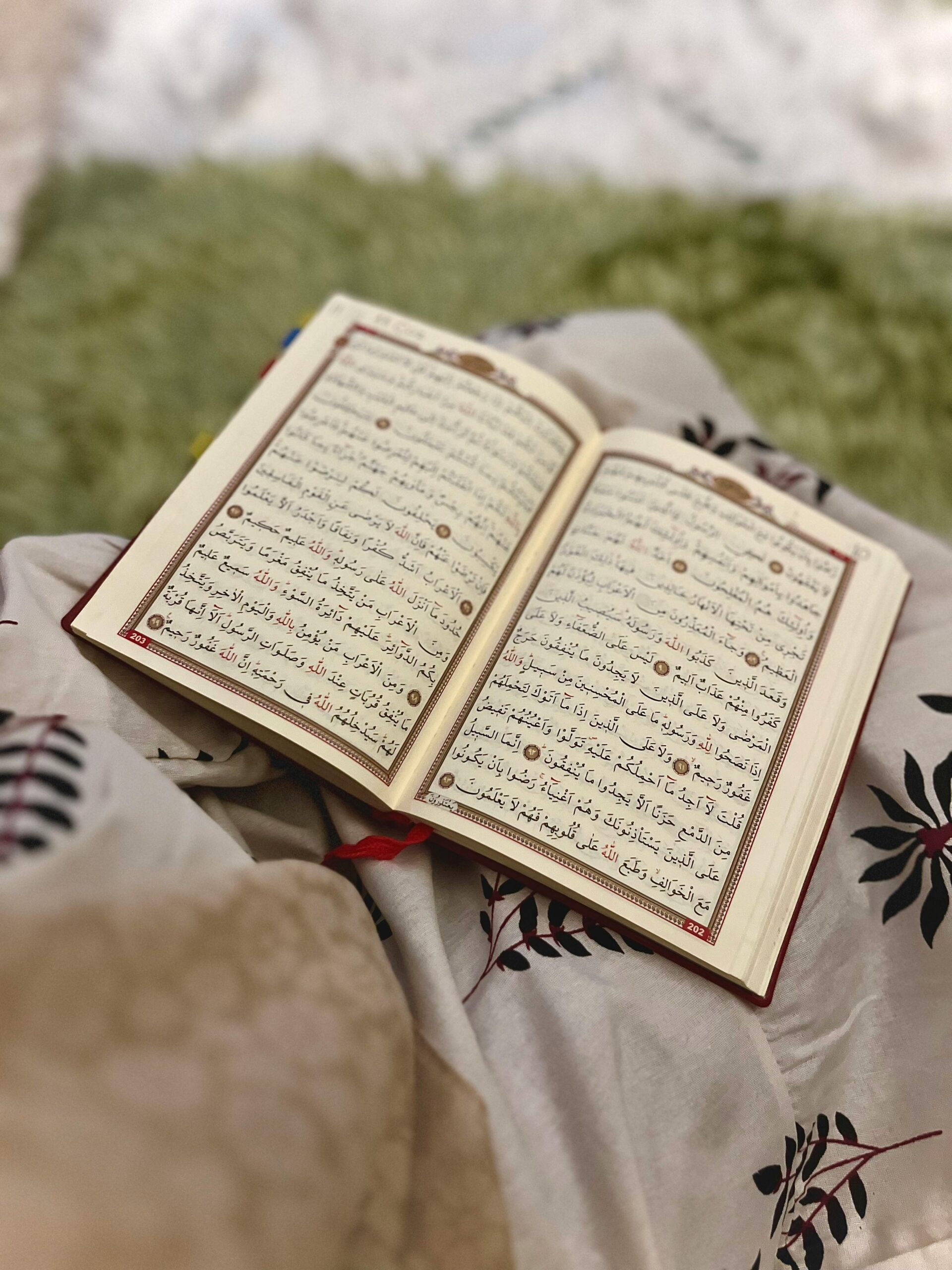 An open Quran resting on a patterned floral blanket, with Arabic text visible.
