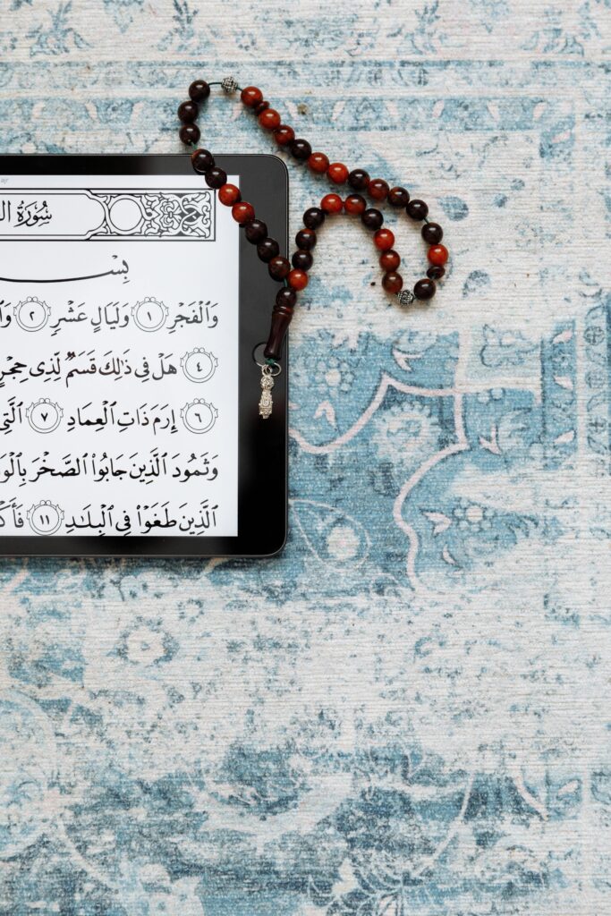 A tablet displaying the Quran on a prayer rug with prayer beads beside it.