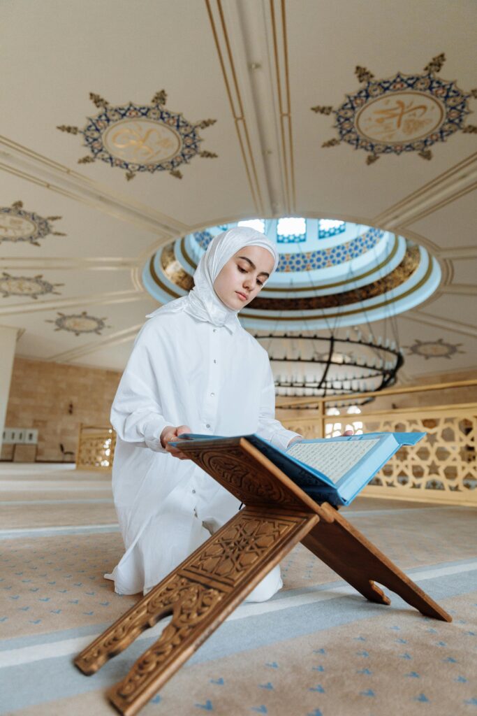 A young woman reading the Quran in a beautifully decorated mosque, symbolizing faith and spirituality.